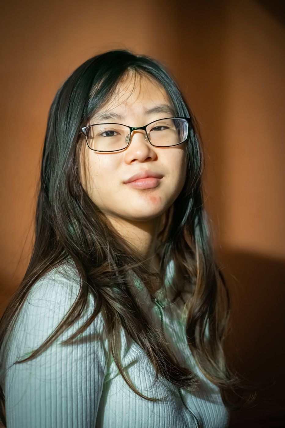 Senior portrait of a young woman with glasses against a warm orange wall