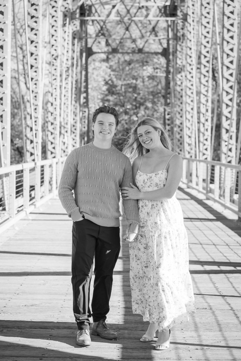 Black-and-white photo of a smiling couple on a steel truss bridge