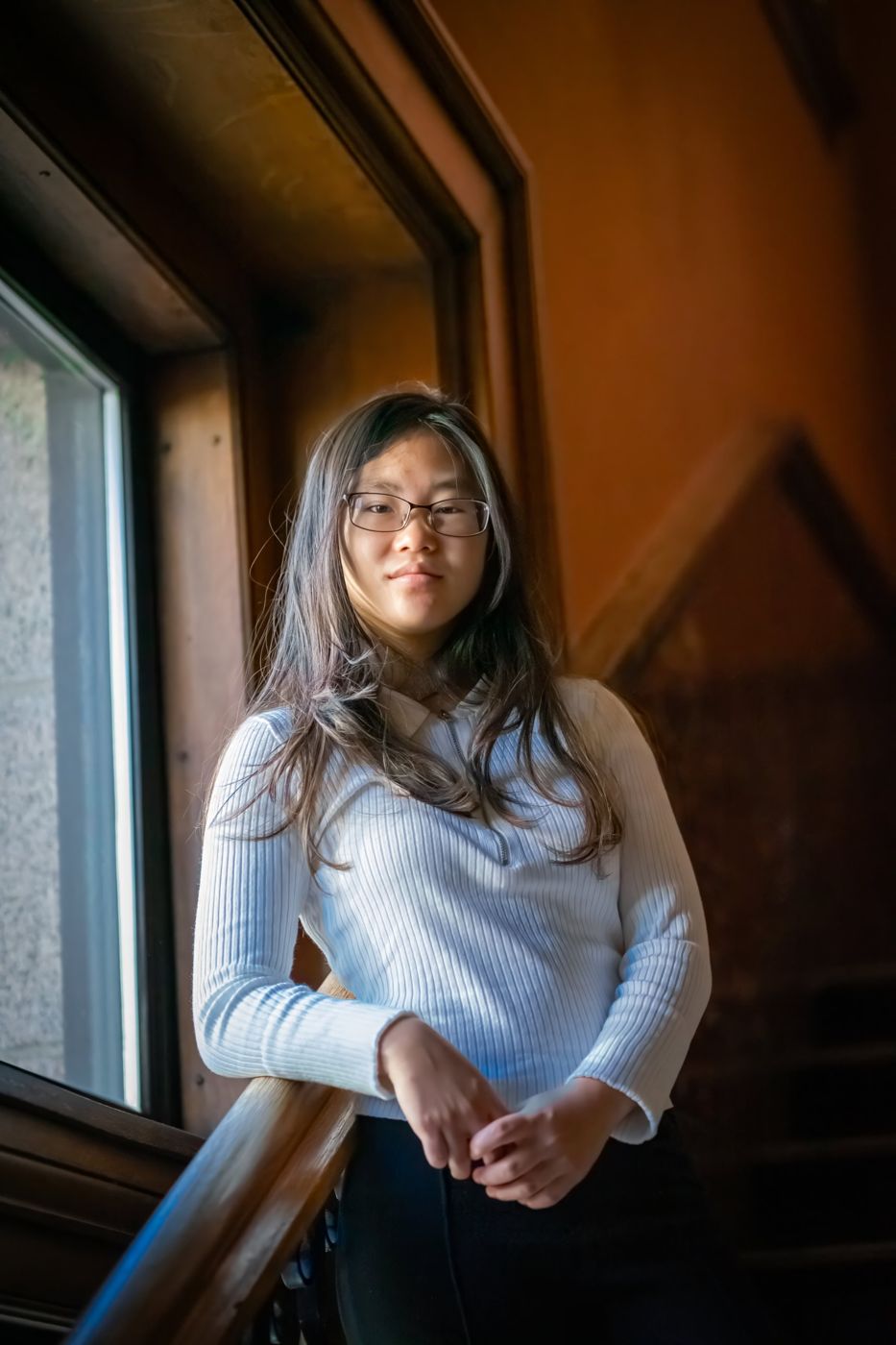 Senior portrait of a young woman by a wood-framed window